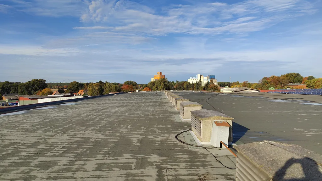 Weites Hallendach mit erneuerter Abdichtung, dahinter Felder und Silos