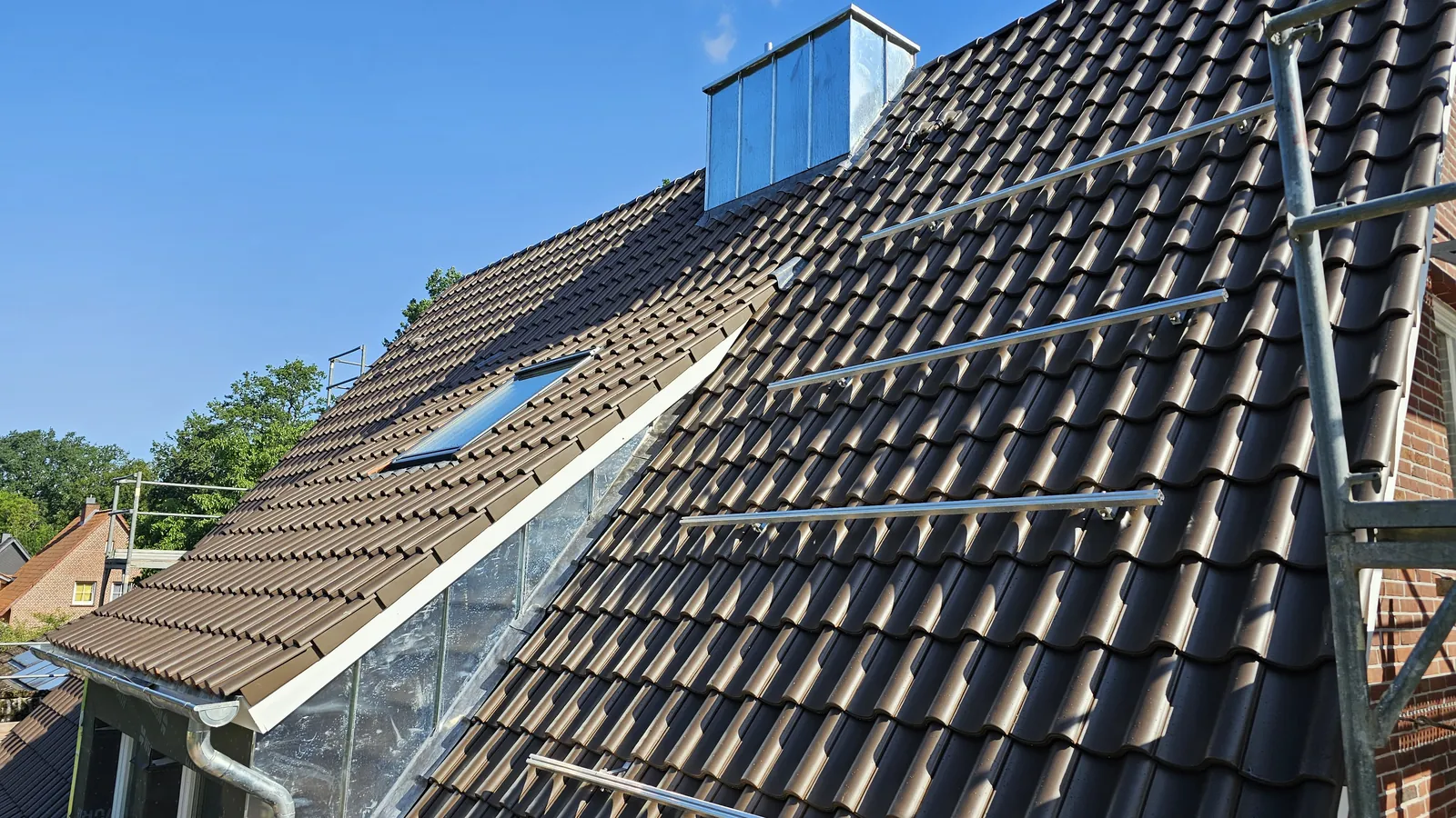 Frisch eingedecktes Steildach mit Kaminverkleidung aus Zink, Dachfenster und Schneefanggittern